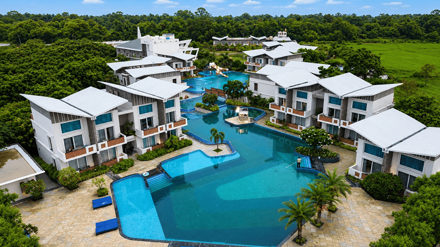 An aerial view of Hotel Sonar Bangla, Mayapur, featuring a central swimming pool, multiple accommodation blocks, palm trees, and green lawns.