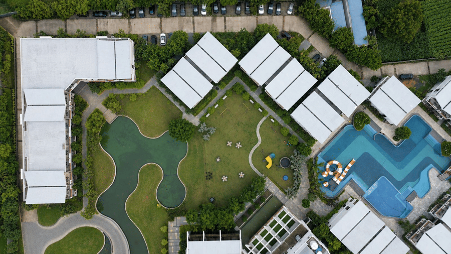 An aerial view of Hotel Sonar Bangla, Mayapur, featuring accommodation buildings, a swimming pool, lawns, and a water body.