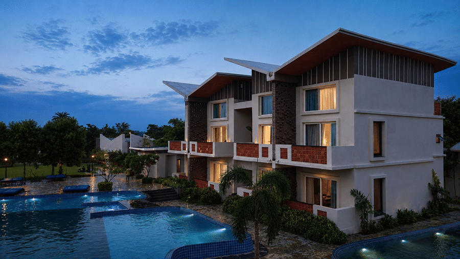 An evening view of guest buildings at Hotel Sonar Bangla, Mayapur, featuring illuminated windows, balcony railings, and a swimming pool.
