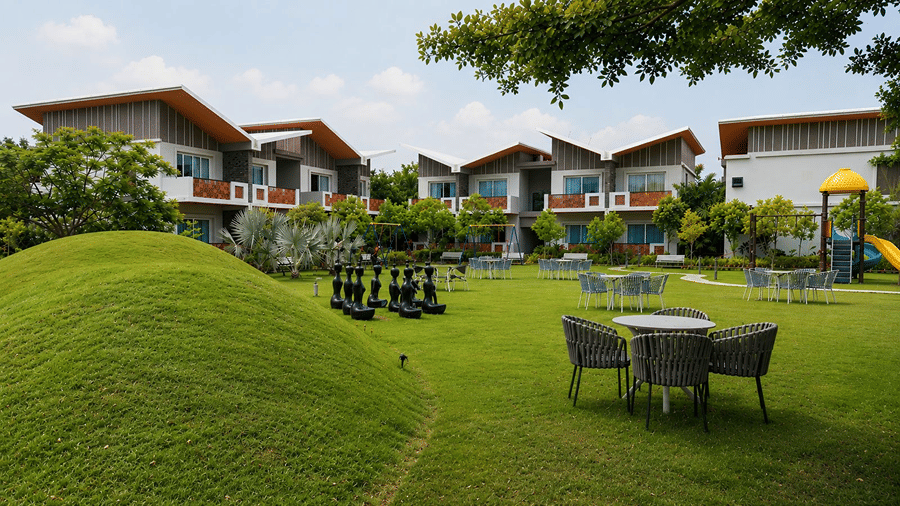 A green lawn at Hotel Sonar Bangla, Mayapur, featuring outdoor seating sets, giant chess pieces, and resort accommodation blocks.