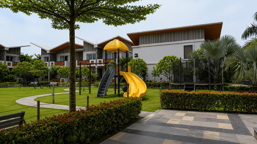 A children playground at Hotel Sonar Bangla, Mayapur, featuring a slide play structure, a paved walkway, and surrounding trees.