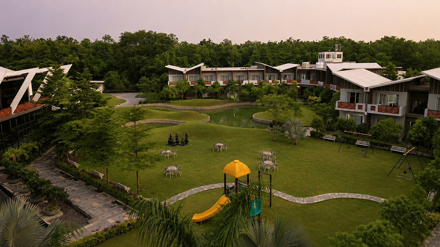 An elevated landscape view at Hotel Sonar Bangla, Mayapur, featuring a green lawn, play equipment, water channels, and trees.