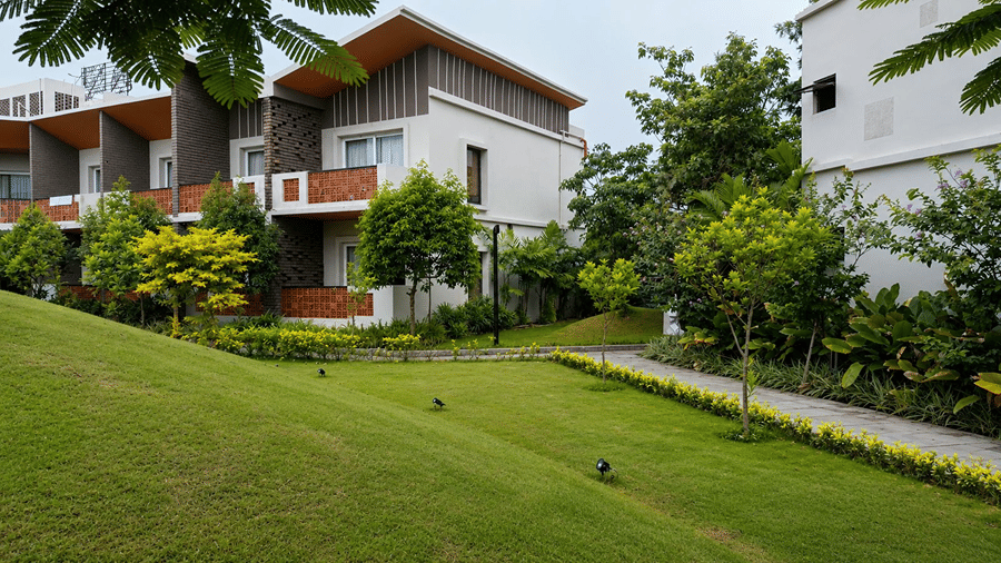 A lawn area at Hotel Sonar Bangla, Mayapur, featuring a grassy mound, a paved foot path, and guest room buildings.