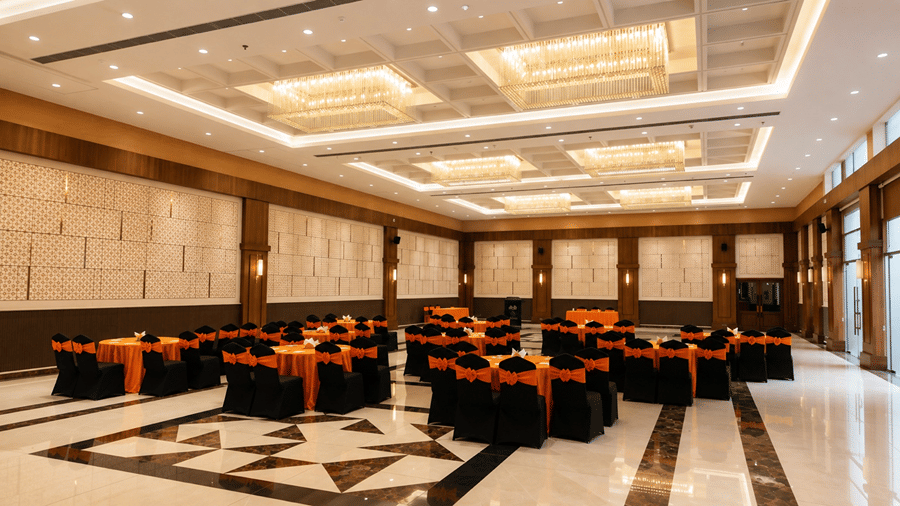 A spacious banquet hall at Hotel Sonar Bangla, Susunia featuring arranged round tables, cushioned chairs, tiled flooring, and decorative ceiling lights.