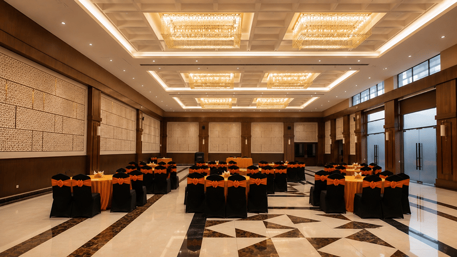 A large banquet hall at Hotel Sonar Bangla, Susunia featuring formal table settings, padded chairs, decorative ceilings, and marble flooring. 
