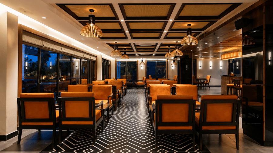 A lounge seating area at Hotel Sonar Bangla, Susunia featuring leather armchairs, patterned floor tiles, wooden ceiling panels, and glass windows.