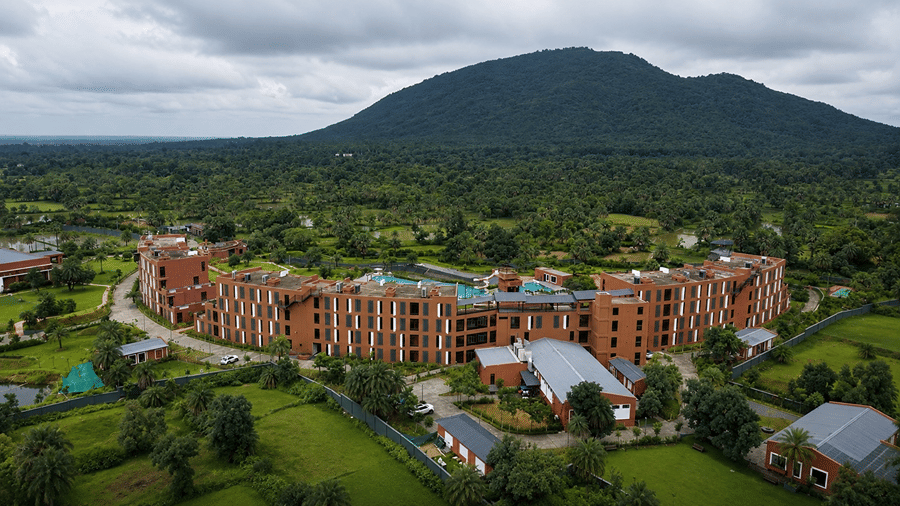 An elevated landscape view of Hotel Sonar Bangla, Susunia featuring brick resort wings, green forest trees, and Susunia Hill in the background.