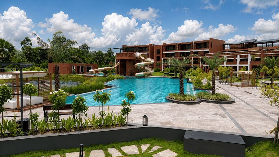 A poolside area at Hotel Sonar Bangla, Susunia featuring a swimming pool, sun deck loungers, shaded cabanas, and potted plants.