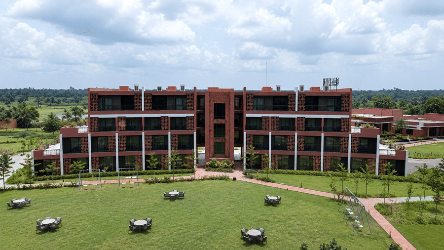A front view of Hotel Sonar Bangla, Susunia featuring brick accommodation wings, balconies, landscaped gardens, and lawn seating.