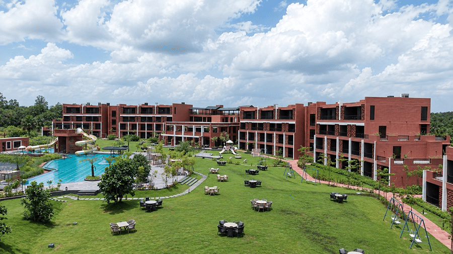 A high-angle view of Hotel Sonar Bangla, Susunia featuring expansive lawns, outdoor dining tables, resort wings, swimming pool, and children play area.