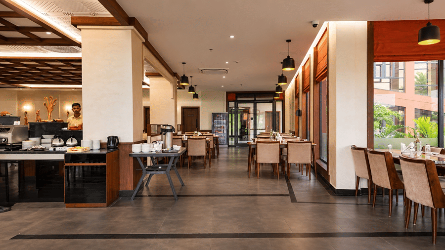An indoor restaurant at Hotel Sonar Bangla, Susunia featuring set dining tables, upholstered chairs, tiled flooring, and hanging lamps.