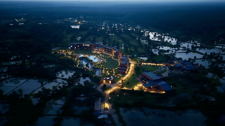 A distant aerial view at dusk of Hotel Sonar Bangla, Susunia featuring lit resort buildings, outdoor lighting, and surrounding countryside.