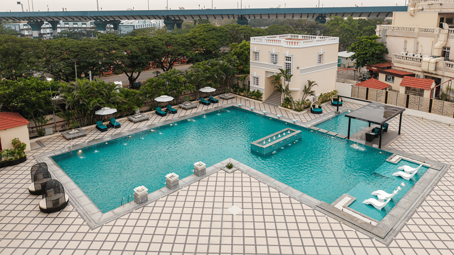 Overview of a clear blue outdoor swimming pool with umbrella-shaded lounge chairs at Jenneys Residency.