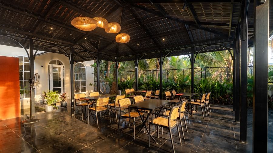 Spacious covered dining area with stylish lighting, offering views of the garden and swimming pool at Kssemya.