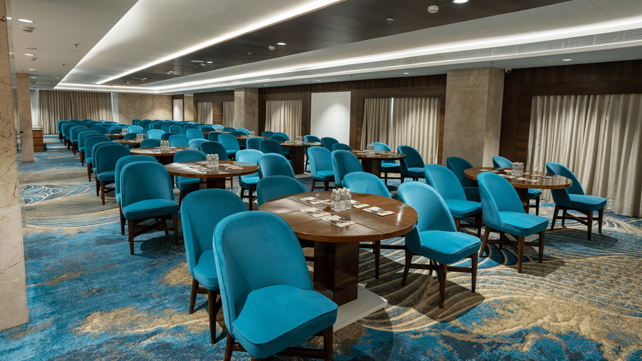 A banquet hall featuring a mix of round and long wooden tables with vibrant teal seating - Praveg's Grand Eulogia, Ahmedabad