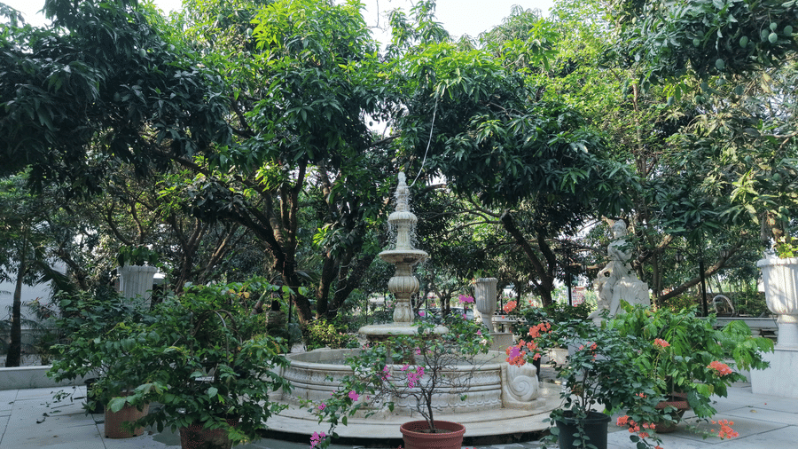 A stone fountain surrounded by lush green trees and potted plants in a resort garden.