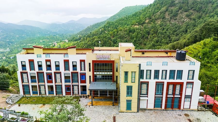 A colourful building complex is nestled in a mountainous, green landscape under a bright sky | Sukama Resort & Spa, Nainital