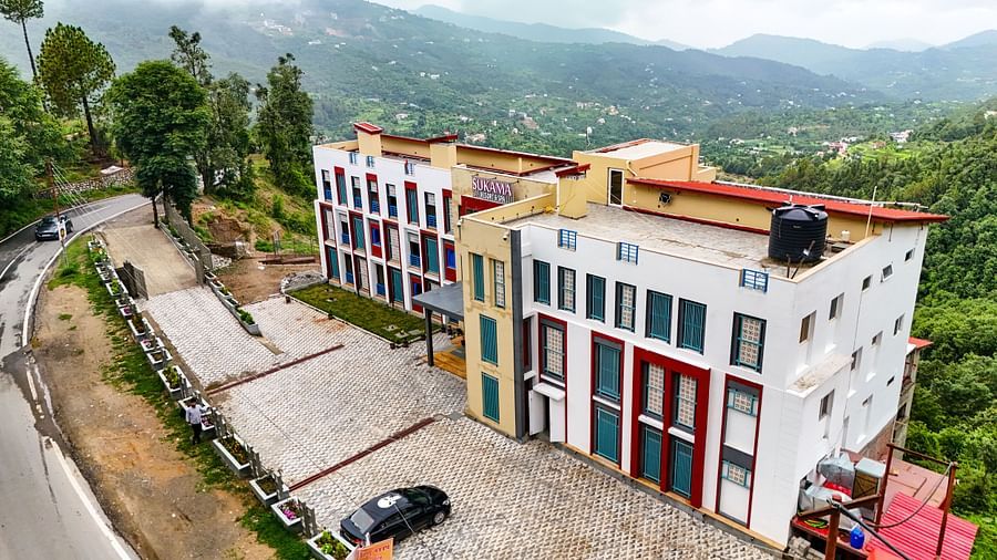 An aerial shot captures a cluster of buildings with distinct architecture amidst a sprawling green landscape | Sukama Resort & Spa, Nainital