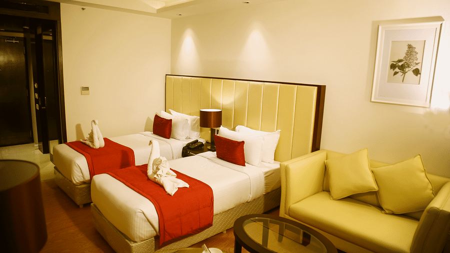 A hotel room furnished with twin beds, each covered with a red throw, and an olive green sofa situated to the side - TGI Grand Fortuna, Hosur