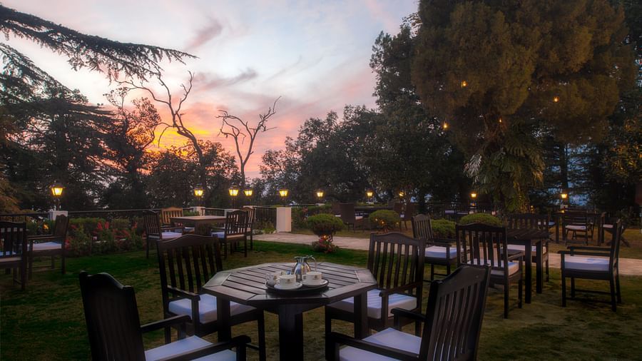outdoor dining area with tables and chairs with the backdrop of a sunset at the Claridges Nabha Residence, Mussoorie