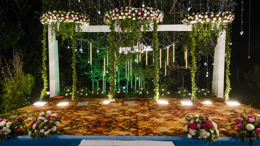 A beautifully decorated wedding stage with a white structure, green foliage, pink flowers, and a reflective floor for a night function at Vedikant Resorts The Mallard Corbett.