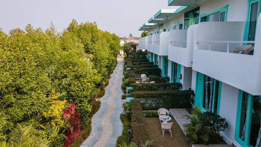 Exterior view of the rooms at Vedikant Resorts The Mallard Corbett featuring two storeys, each room with a balcony, a bunch of trees outside and seating area under each building.