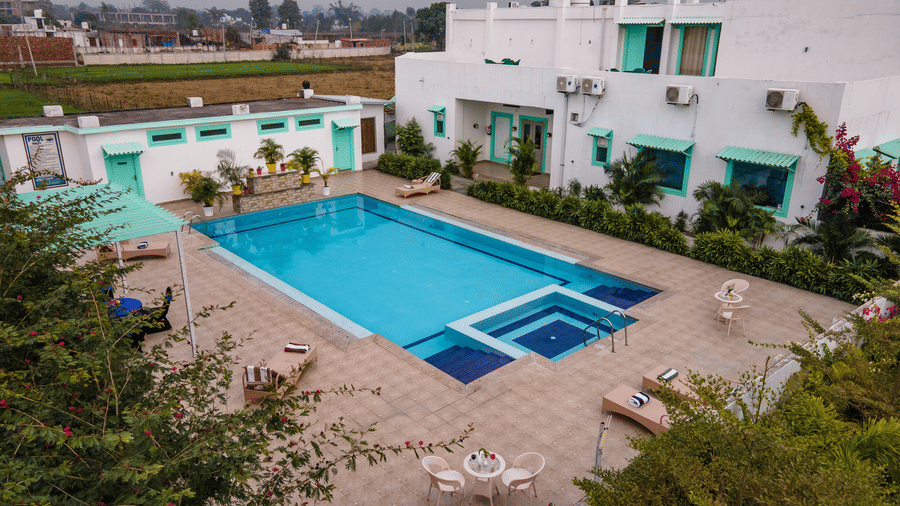 facade of Vedikant Resorts The Mallard Corbett featuring a sprawling pool with loungers and tables, all nestled within a lush, two-story forest retreat