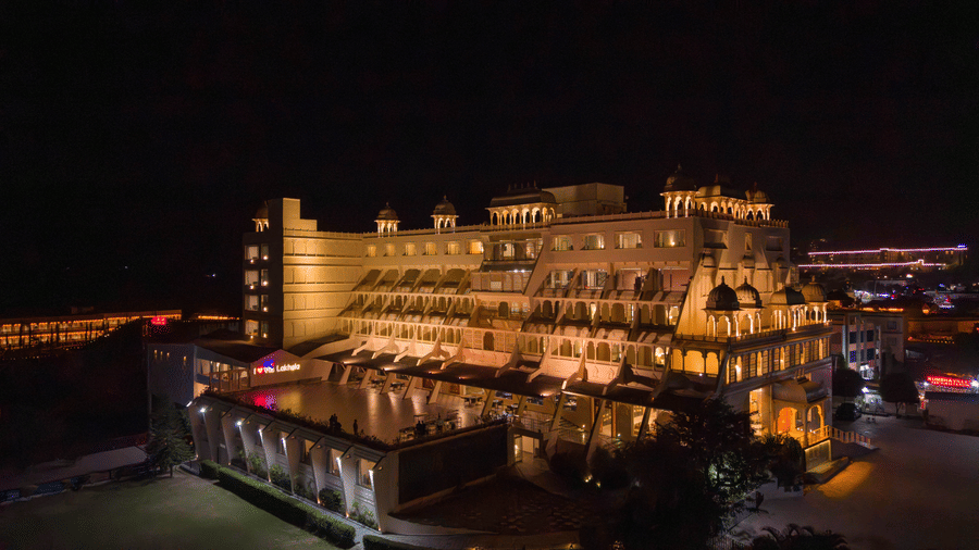An evening drone view of Via Lakhela Lakeview Resort, highlighting the grand illuminated facade, waterfront deck, and vibrant lighting across the property.