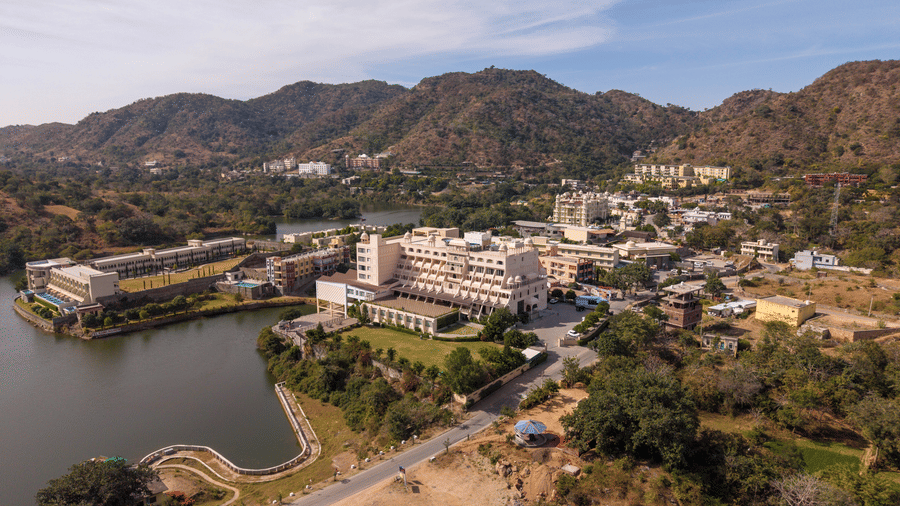 An aerial view of Via Lakhela Lakeview Resort, showcasing the resort buildings along the lakeshore, with rugged hills and natural surroundings in the background.