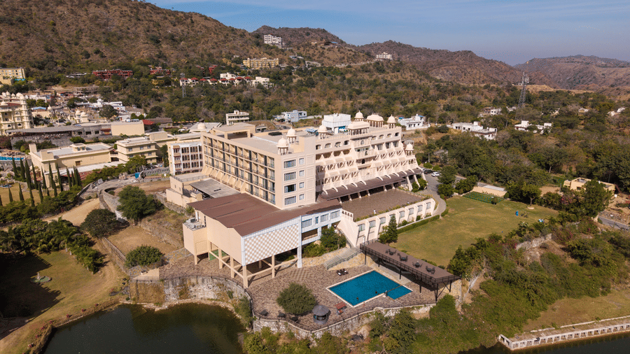 An elevated aerial view of Via Lakhela Lakeview Resort, highlighting the outdoor swimming pool, lakefront location, and the surrounding hills.