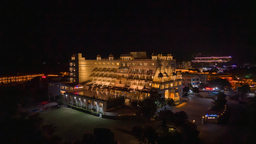 A night-time aerial view of Via Lakhela Lakeview Resort, illuminated with warm lighting along the waterfront, with reflections shimmering across the lake.