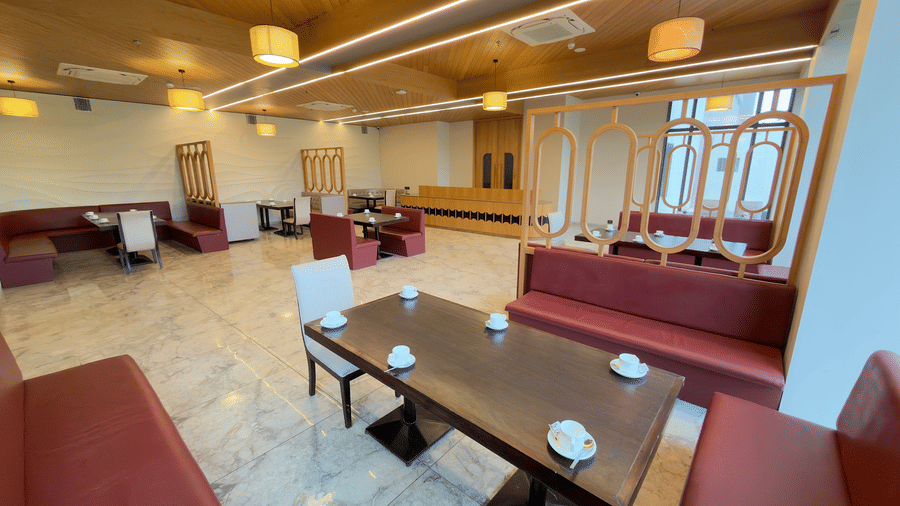 coffee shop in Vinti Resort with a wooden ceiling, warm lighting, red cushioned seating, and glass-topped tables.