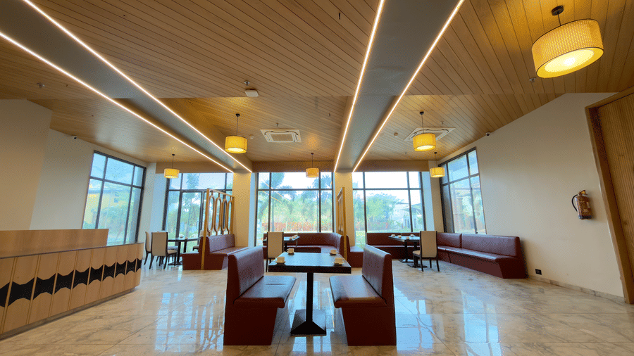 coffee shop in Vinti Resort with warm light and a wooden ceiling, warm lighting, red cushioned seating, and glass-topped tables.