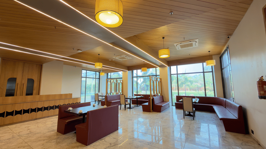 coffee shop in Vinti Resort with a ceiling, warm lighting, red cushioned seating, and glass-topped tables.