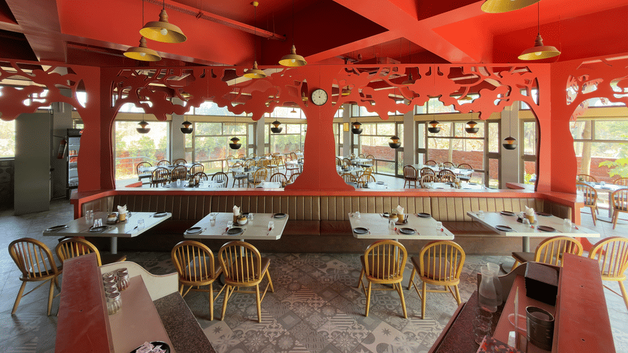 The restaurant at Vinti Resort, Ambaji, warmly lit for dinner, features a decorative ceiling and comfortable tables set for dining.