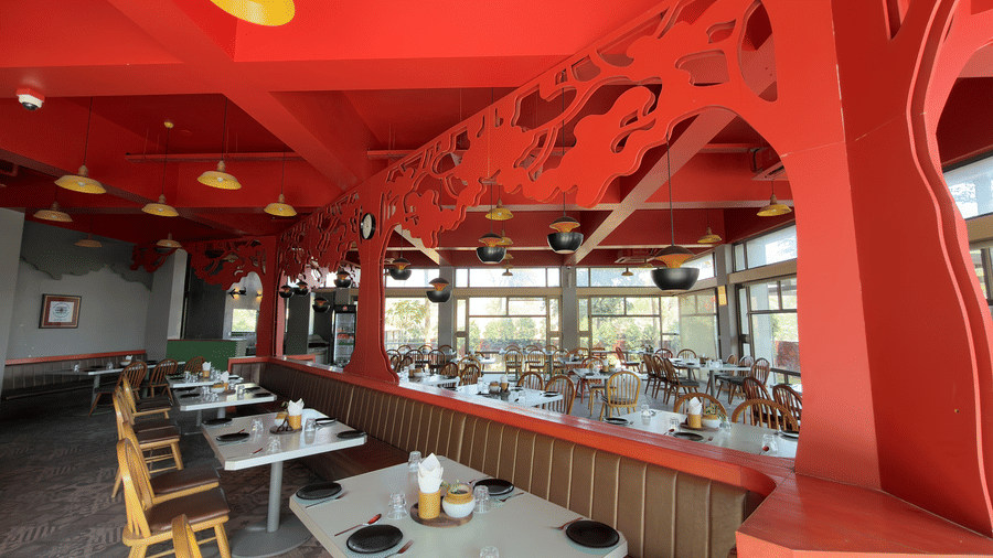 The restaurant at Vinti Resort, Ambaji,  lit for  meals, features a striking pink ceiling and comfortable tables set for dining.