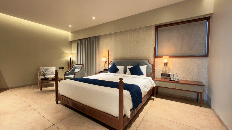 Hotel villa room with bed side tables, wall art, television, chair, desk, curtains, and window showing outdoor view