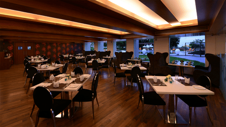 a restaurant area with differently arranged seating area and glass windows to the pool area at Top3 Lords Resort Bhavnagar