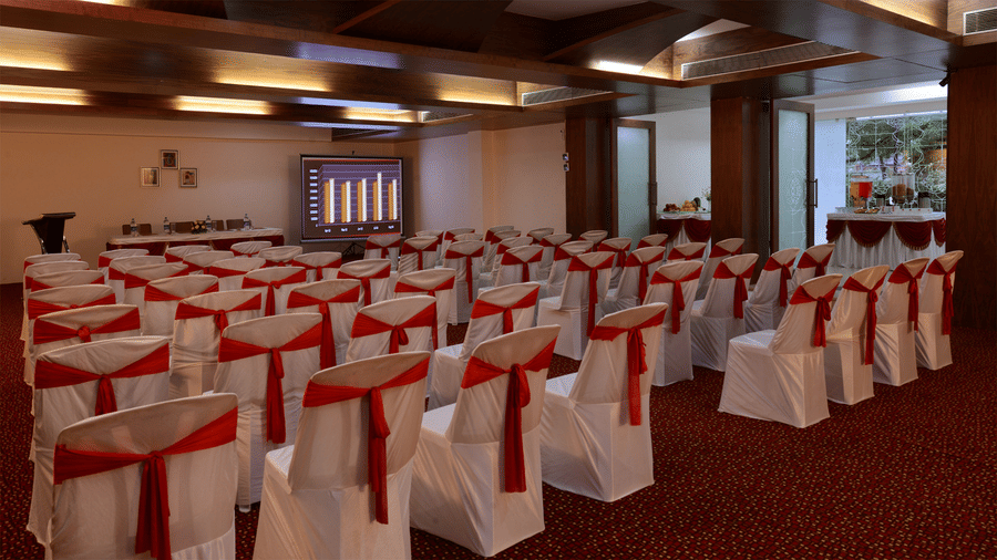 a banquet hall arranged in theatre seating style with warmly lit ceiling lights with a projector and buffet table by the sides at Top3 Lords Resort Bhavnagar