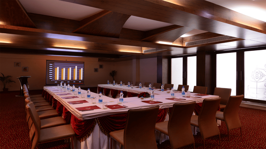 a conference room at Top3 Lords Resort Bhavnagar with a U-shaped seating arrangements with a projector and glass windows  on the side.