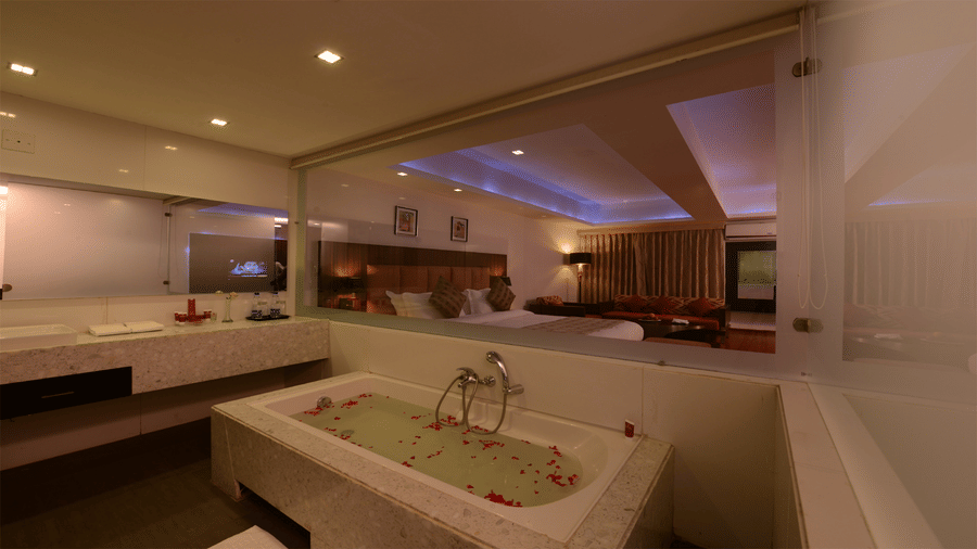 a bathroom in the executive room with a single faucet, amenities, and a bath tub decorated with rose petals overlooking the bed room through the glass window at Top3 Lords Resort Bhavnagar