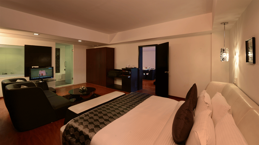 an executive king size bed room with a seat area, a wardrobe, a TV, and an attached bathroom with translucent doors at Top3 Lords Resort Bhavnagar