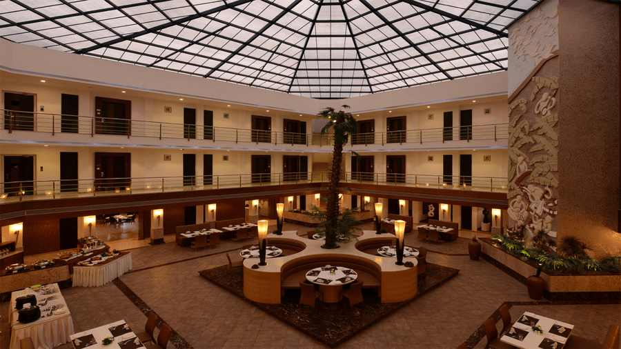 an elegant hotel atrium with glass-domed ceiling  featuring a central dining area surrounded by guest room balconies at Top3 Lords Resort Bhavnagar
