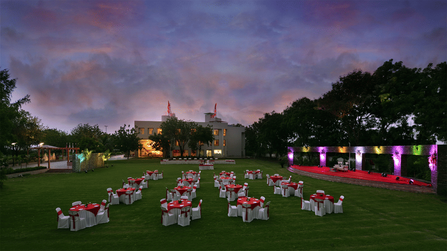 lawn area with neatly arranged seating area in clusters for an event  with a stage on one side and the Top3 Lords Resort Bhavnagar entrance behind