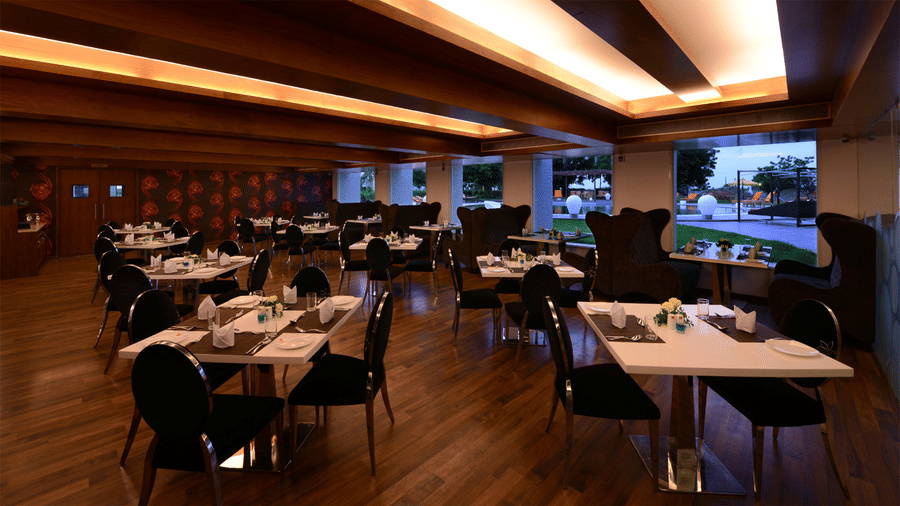 a restaurant area with differently arranged seating area and glass windows to the pool area at Top3 Lords Resort Bhavnagar