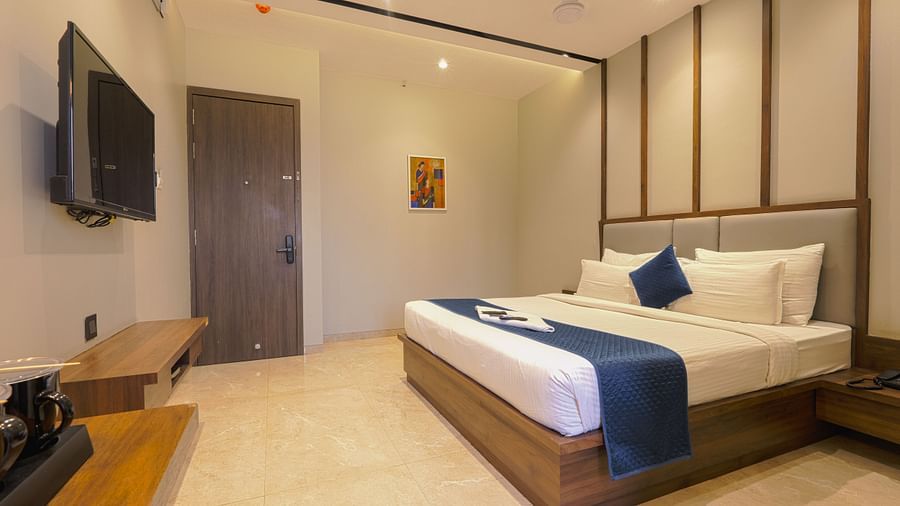 alt-text An image of a bedroom featuring a double size bed, flat TV screen, an AC, a work desk and chair, and a cabinet table below the TV - Magnus Fortune House, Magarpatta
