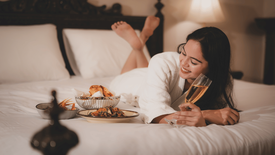 A woman lying on a bed eating from a dining tray placed in front of her at The Suryaa, New Delhi.