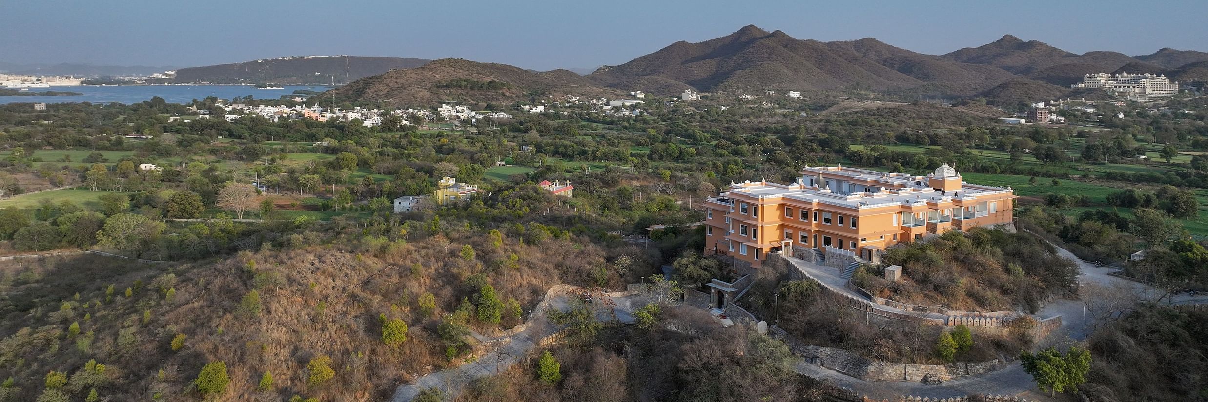 Aerial shot of Khas Mahal by Fateh Collection, Udaipur surrounded by mountains and lush green landscapes.