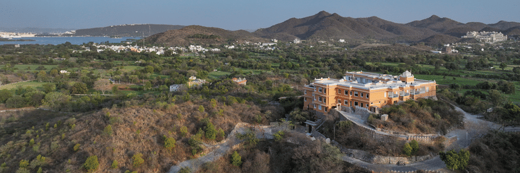 Aerial shot of Khas Mahal Suites, Udaipur surrounded by mountains and lush green landscapes.