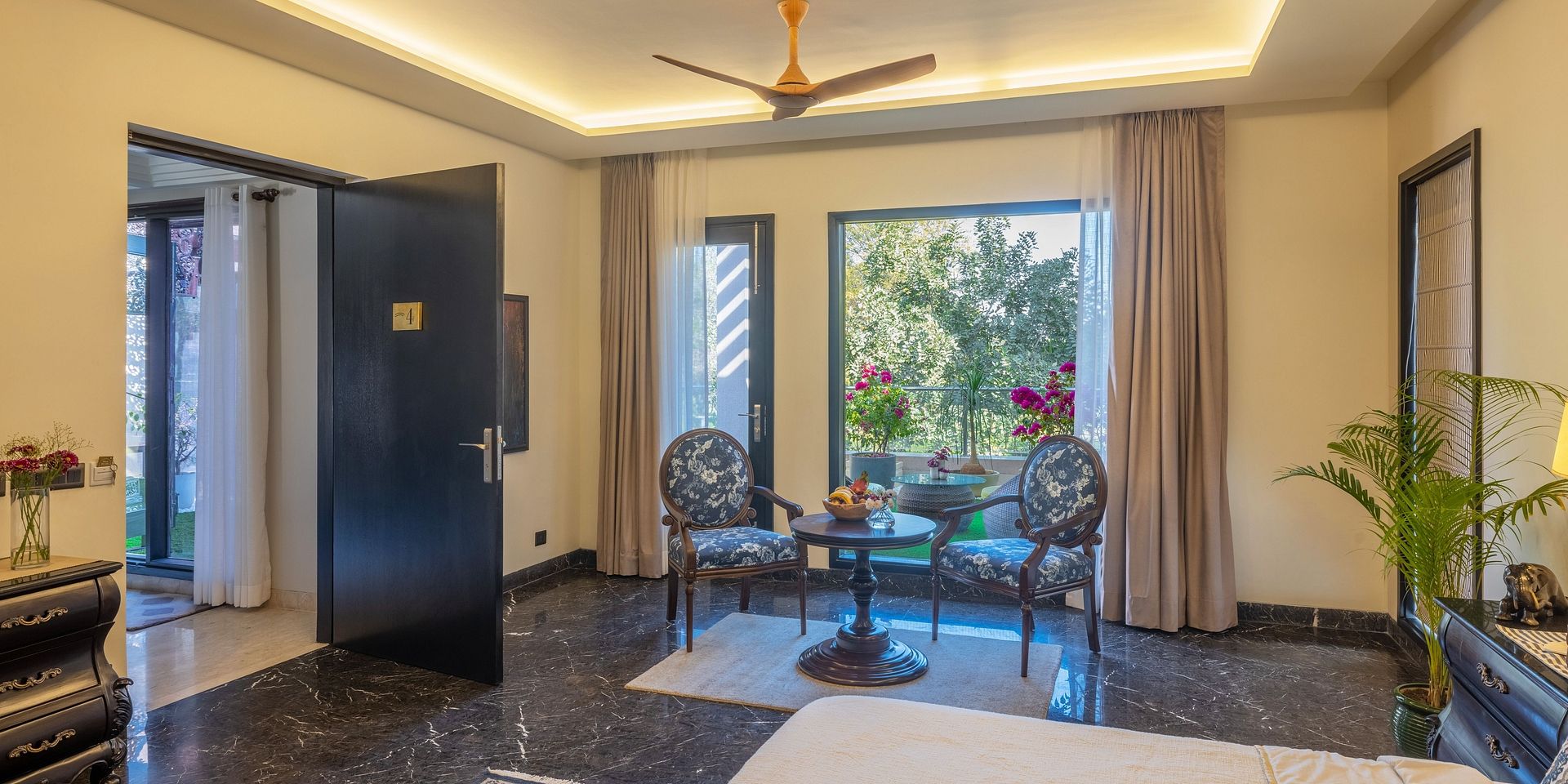 A room at Karma Chalets with a glass door opening to a garden, a table with chairs, and a ceiling fan above.